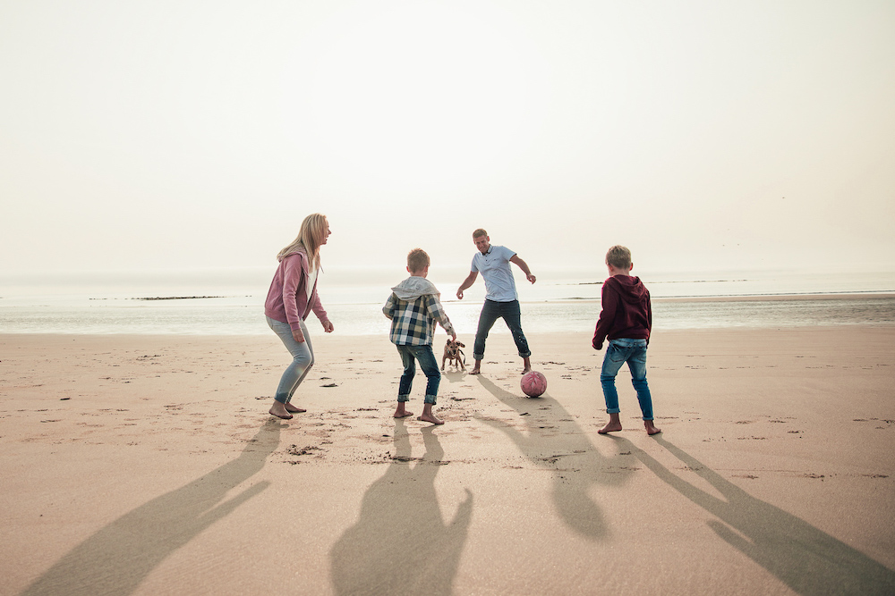 Family With Young Kids And A Dog Playing On The Beach