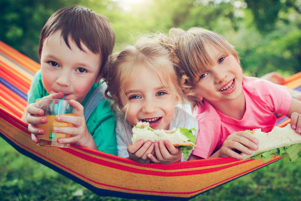 Happy Kids Eating And Drinking In A Hammock