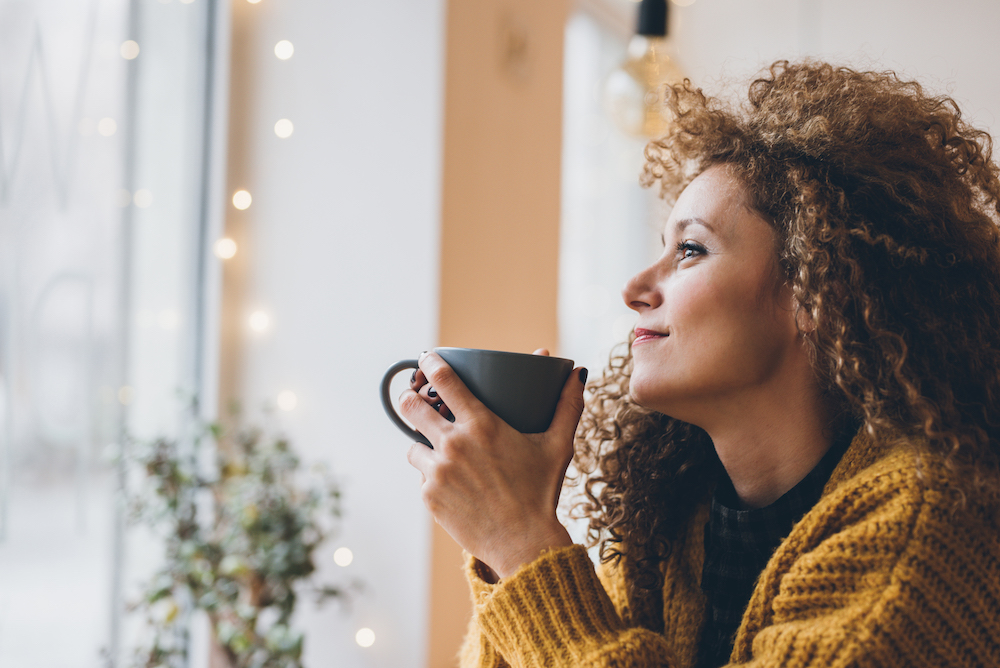 Woman drinking coffee while looking out the window of a coffee shop in fall or winter