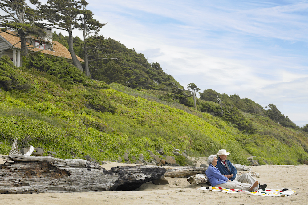 Couple sitting on beach leaning against driftwood log