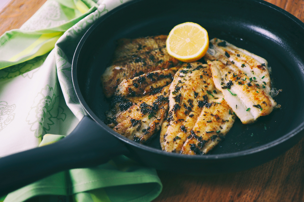 Skillet with fish filets and half of a lemon