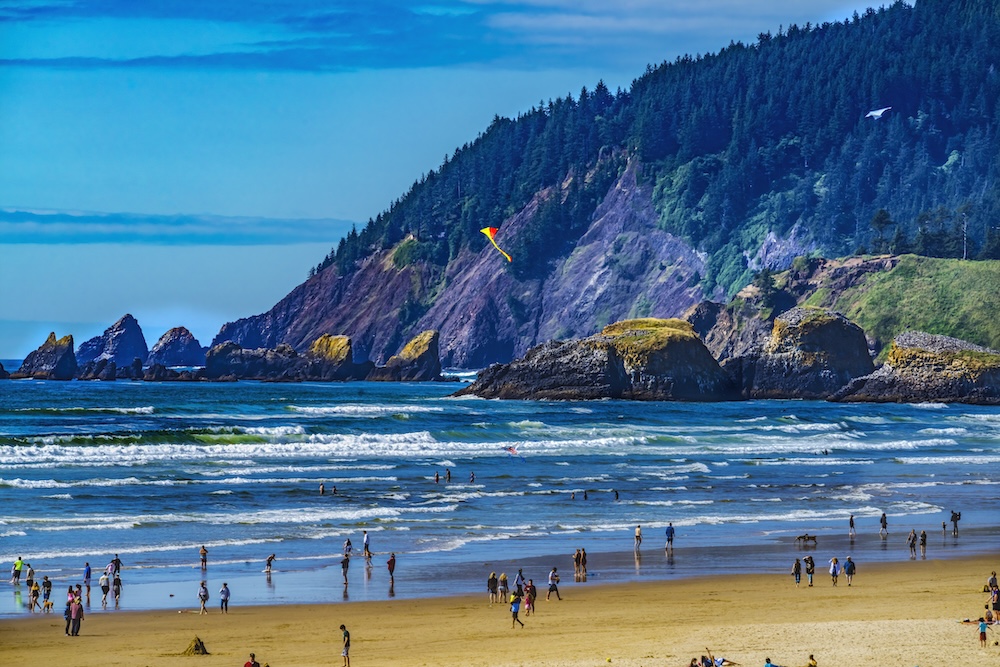 People on beach in Cannon Beach, Oregon. Kite flying in the air overhead.