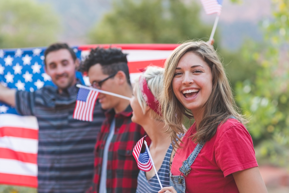 Group of millennial friends hold a large American flag at a fourth of july event